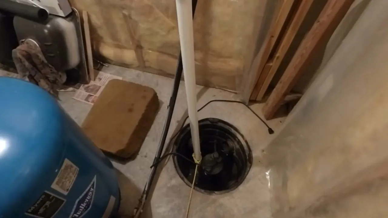 Black sump pump installed in a basement pit beside a pressure tank
