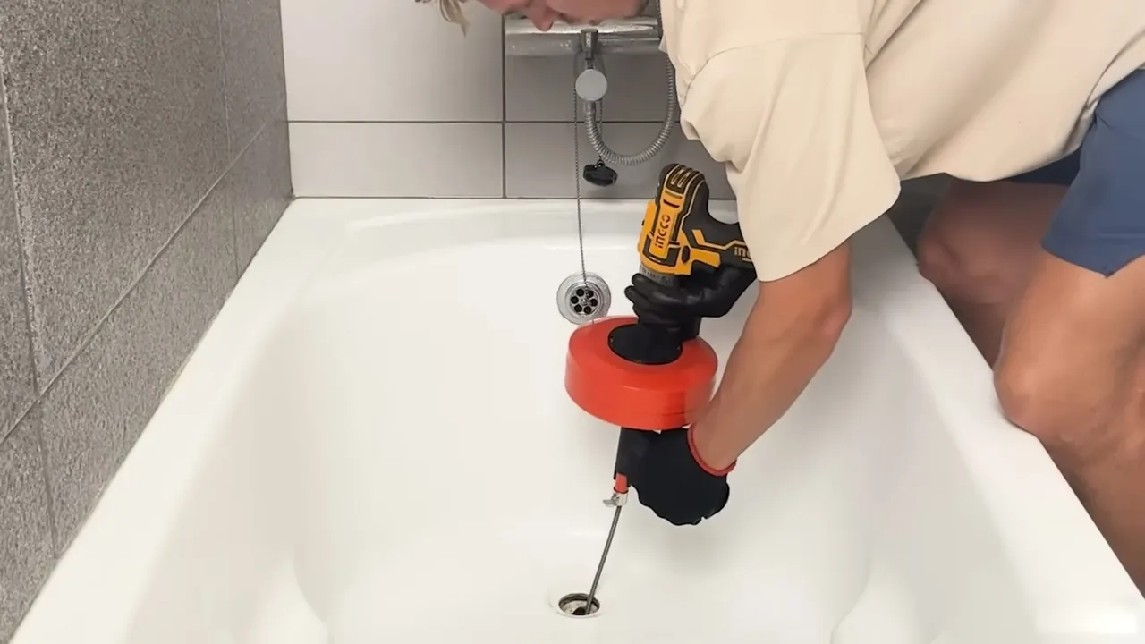 Plumber feeding a drain auger through a bathtub drain opening