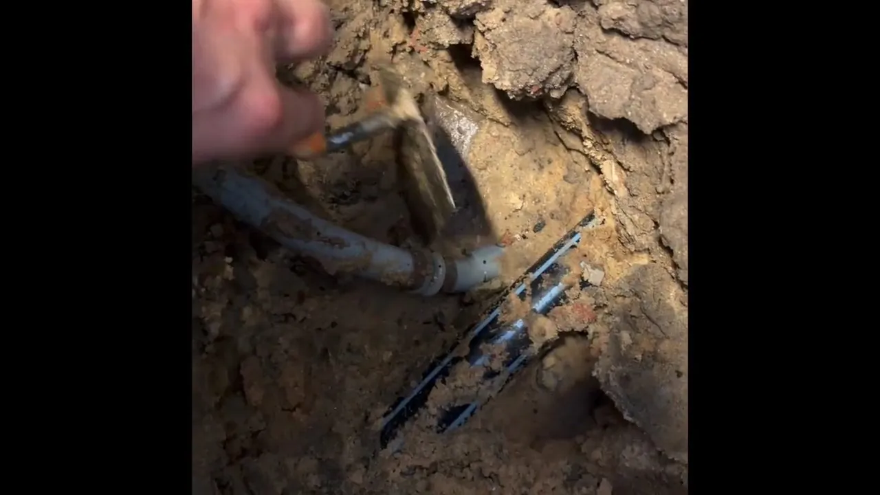 Burst water pipe exposed beneath a broken concrete slab for emergency repair