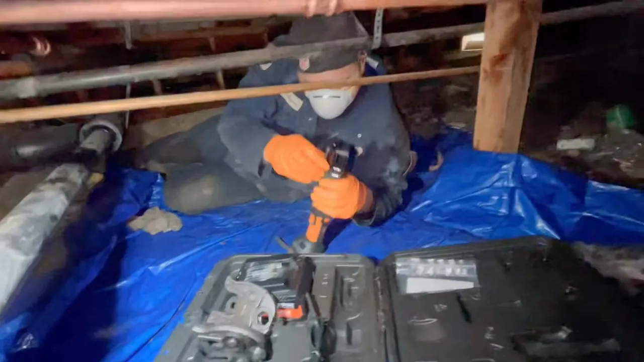 Plumber using repair tools on a water pipe inside a crawlspace