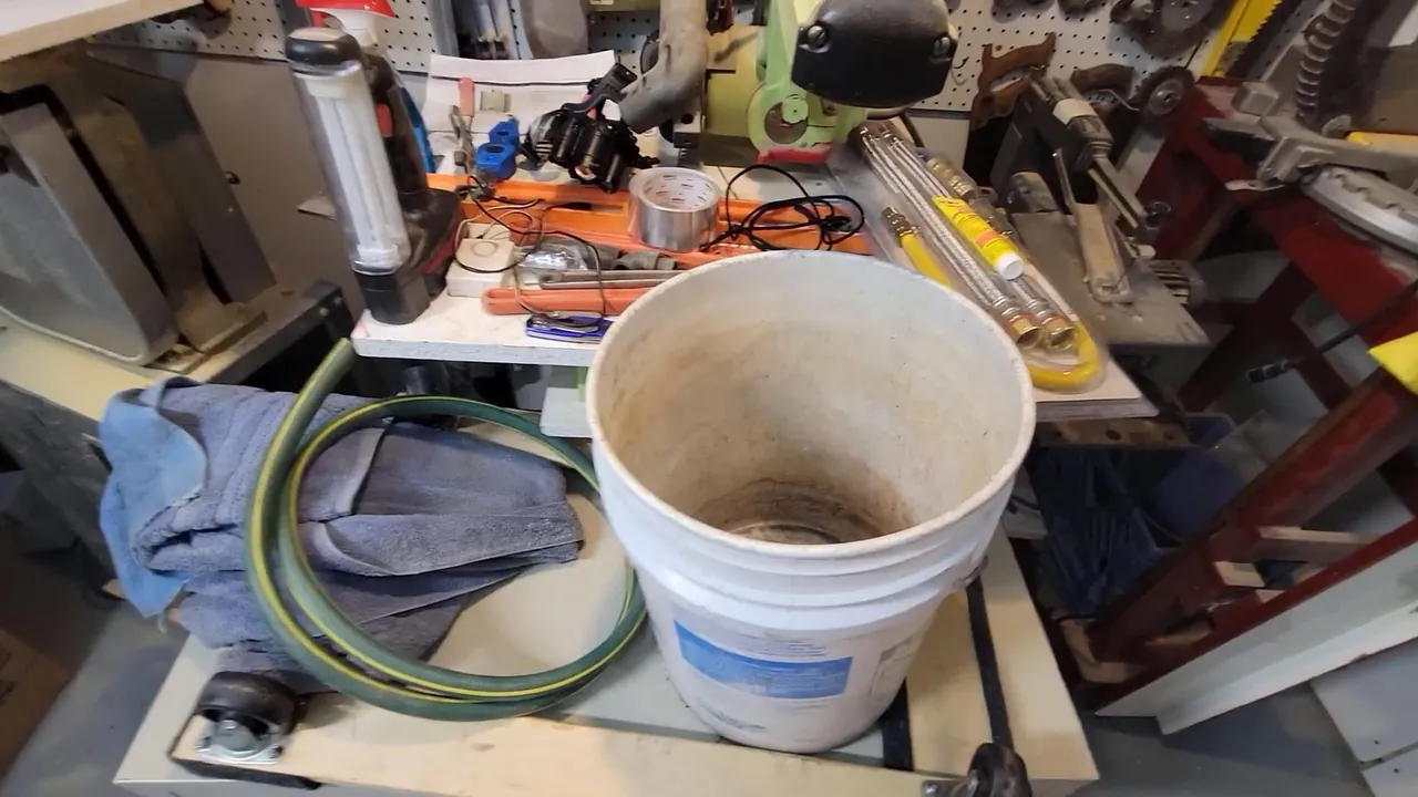 Drain-cleaning hose, collection bucket, and service tools prepared beside a work area