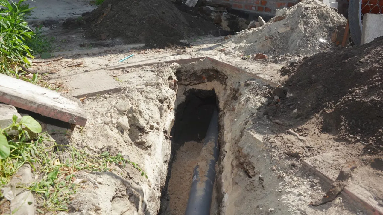 Open sewer repair trench with an underground pipe exposed in compacted soil
