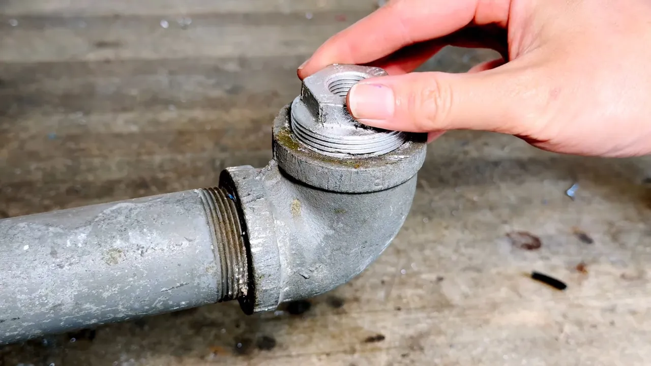 Older galvanized pipe elbow with a threaded cleanout plug and visible wear