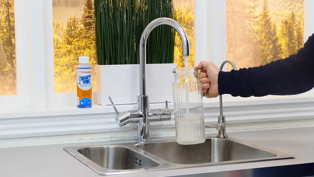 Clear tap water running from a kitchen faucet into a glass container