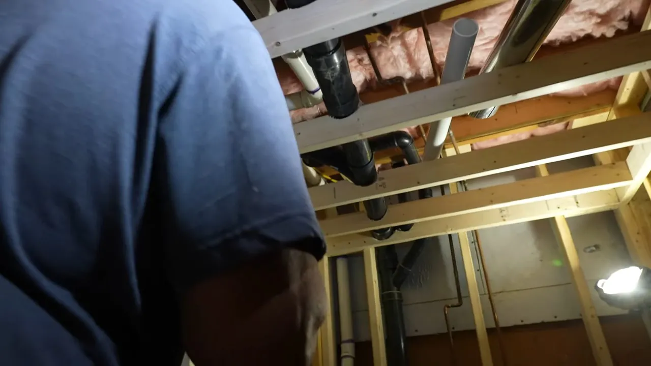 Plumber installing drain and supply piping above an open Sunnyside ceiling